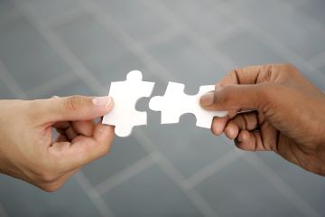 The hands of two people are shown placing two puzzle pieces together.