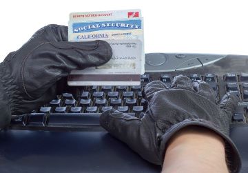 Image of a person's gloved hands holding an assortment of credit cards and personal ID while keying information into a keyboard.