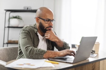 Male concentrating while working on laptop at desk in home office