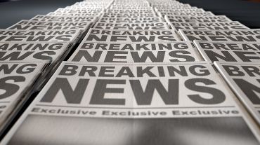 A long row of folded newspapers at the end of a press run with a generic headline that reads breaking news on the front page
