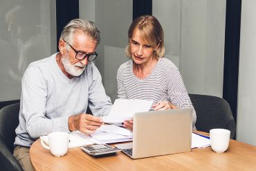Senior couple reading documents and calculating bills to pay in living room at home