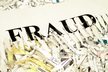 this is an image of the word fraud run through a paper shredder and laying on a pile of shredded paper.
