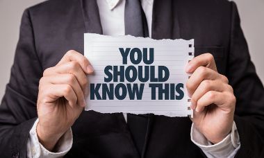 Business person in a suit holds up a torn piece of paper with the words You Should Know This.