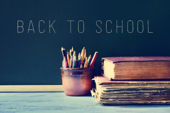 some pencils in a pot, some old books on a blue school desk, and the text back to school written on a chalkboard
