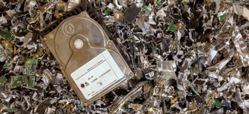 A metallic hard drive sitting on top of a pile of scrap metal, likely destroyed hard drives