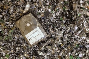 A metallic hard drive sitting on top of a pile of scrap metal, likely destroyed hard drives