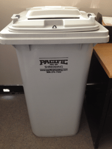 A grey secure collection container with a Pacific Shredding Label